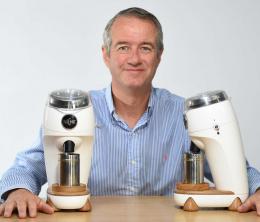 Martin Nicholson sitting at a table on which sits two examples of his Niche Zero Grinder