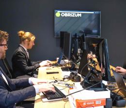 Three members of the OBRIZUM R&D and Product team working at a table with OBRIZUM-branded pop-up stand in the backgroundan
