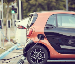 Orange and black Smart car being recharged at street side.