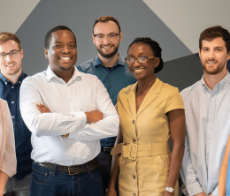Founders Neciah and Josephine Dorh surrounded by three male and three females members of the FluoretIQ team posing against a grey diagrammatic office background..