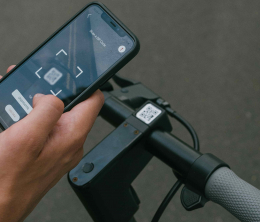 A man's hand on a mobile displaying an app fixed to handlebars of an electric scooter.