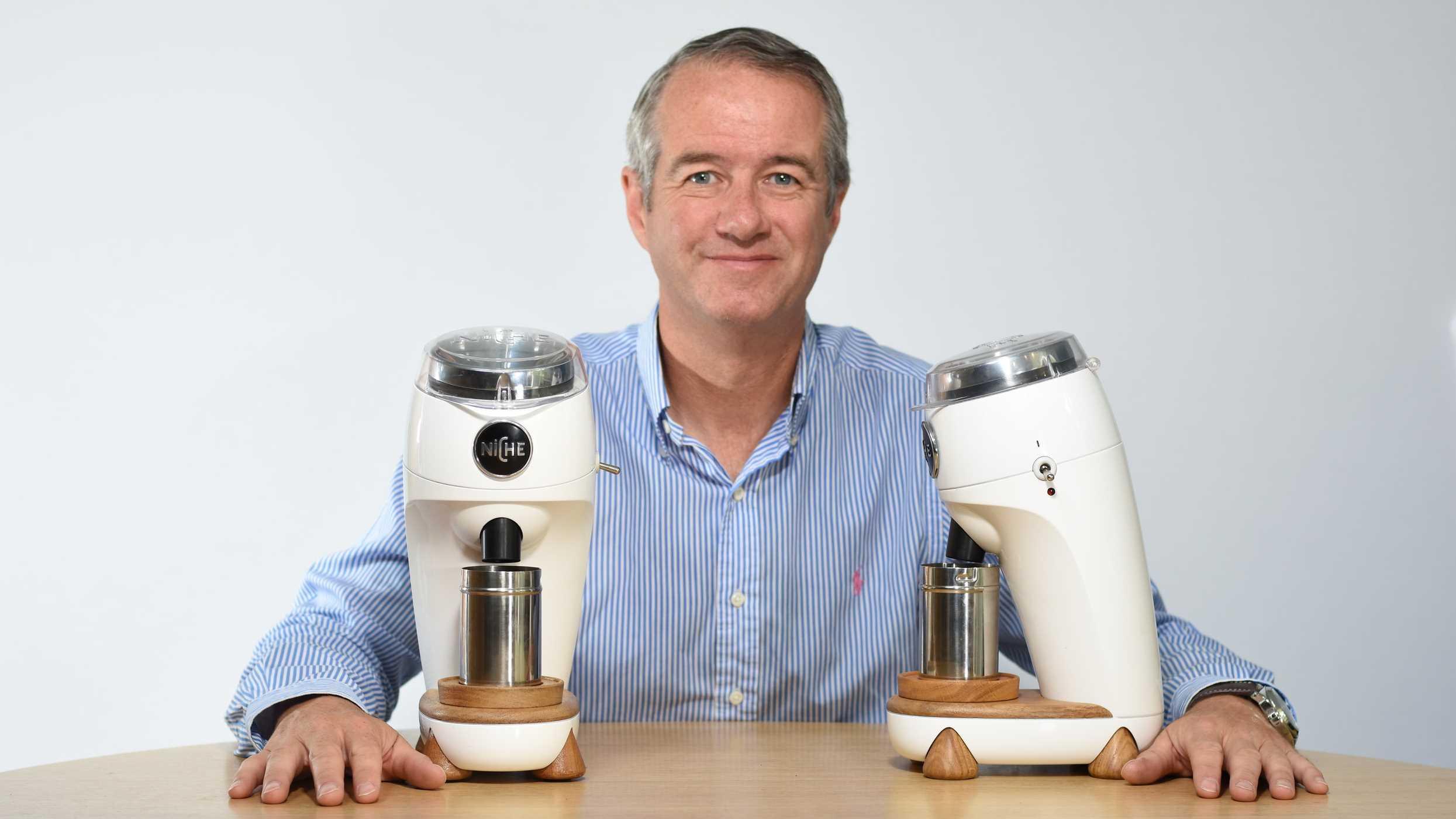 Martin Nicholson sitting at a table on which sits two examples of his Niche Zero Grinder