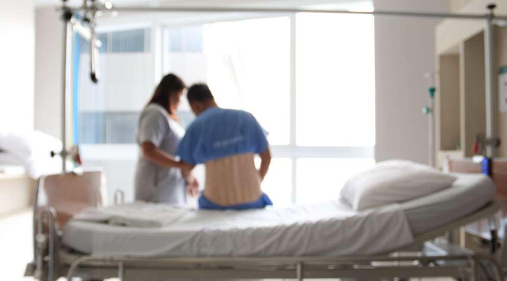 Image (blurred) of patient sitting on hospital bed with nurse standing.