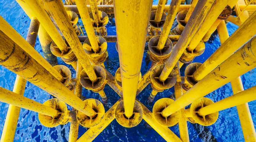 Overhead picture of yellow oil and gas pipework on an offshore wellhead remote platform, with blue sea.