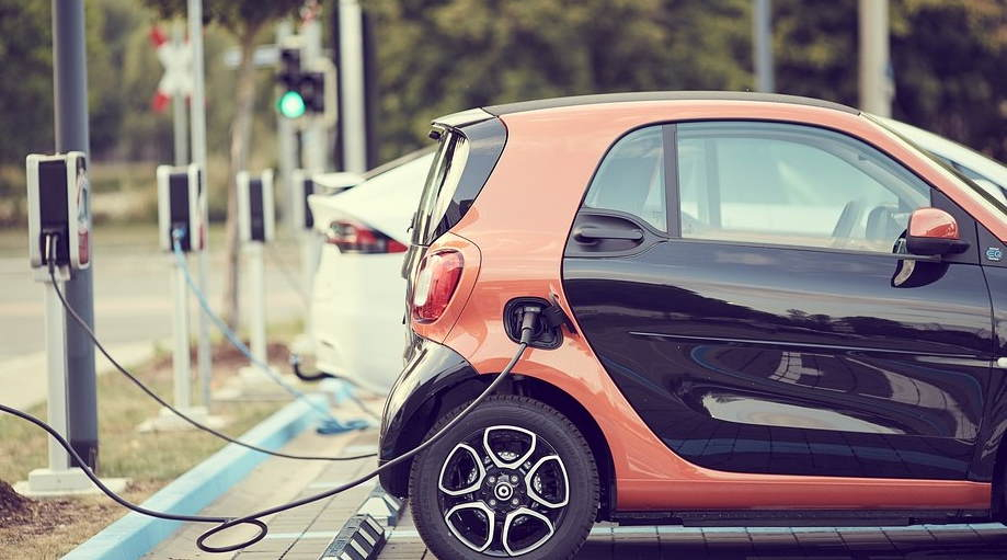Orange and black Smart car being recharged at street side.