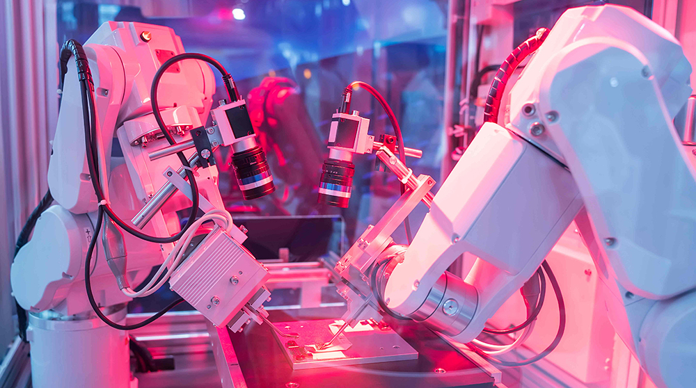 Two robotic manufacturing machines at work in pink lighting.